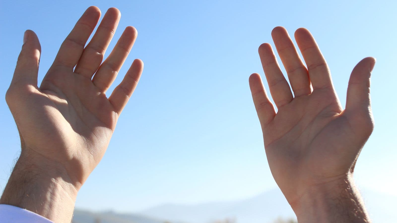 Mains levées pour une invocation devant un ciel bleu