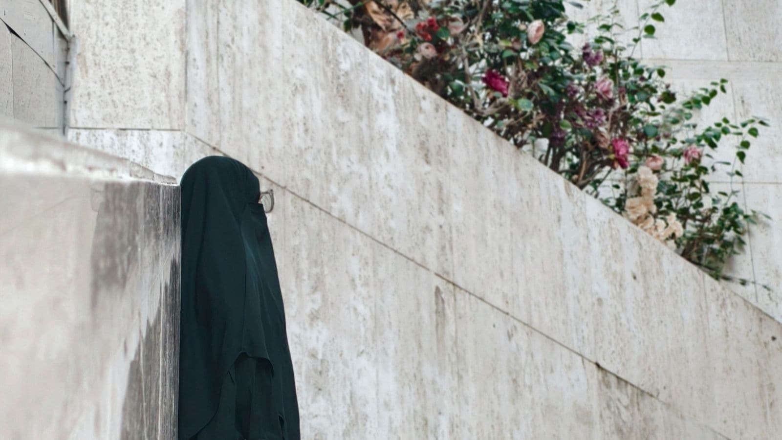 Femme en vêtement noir de dos près d'un mur fleuri