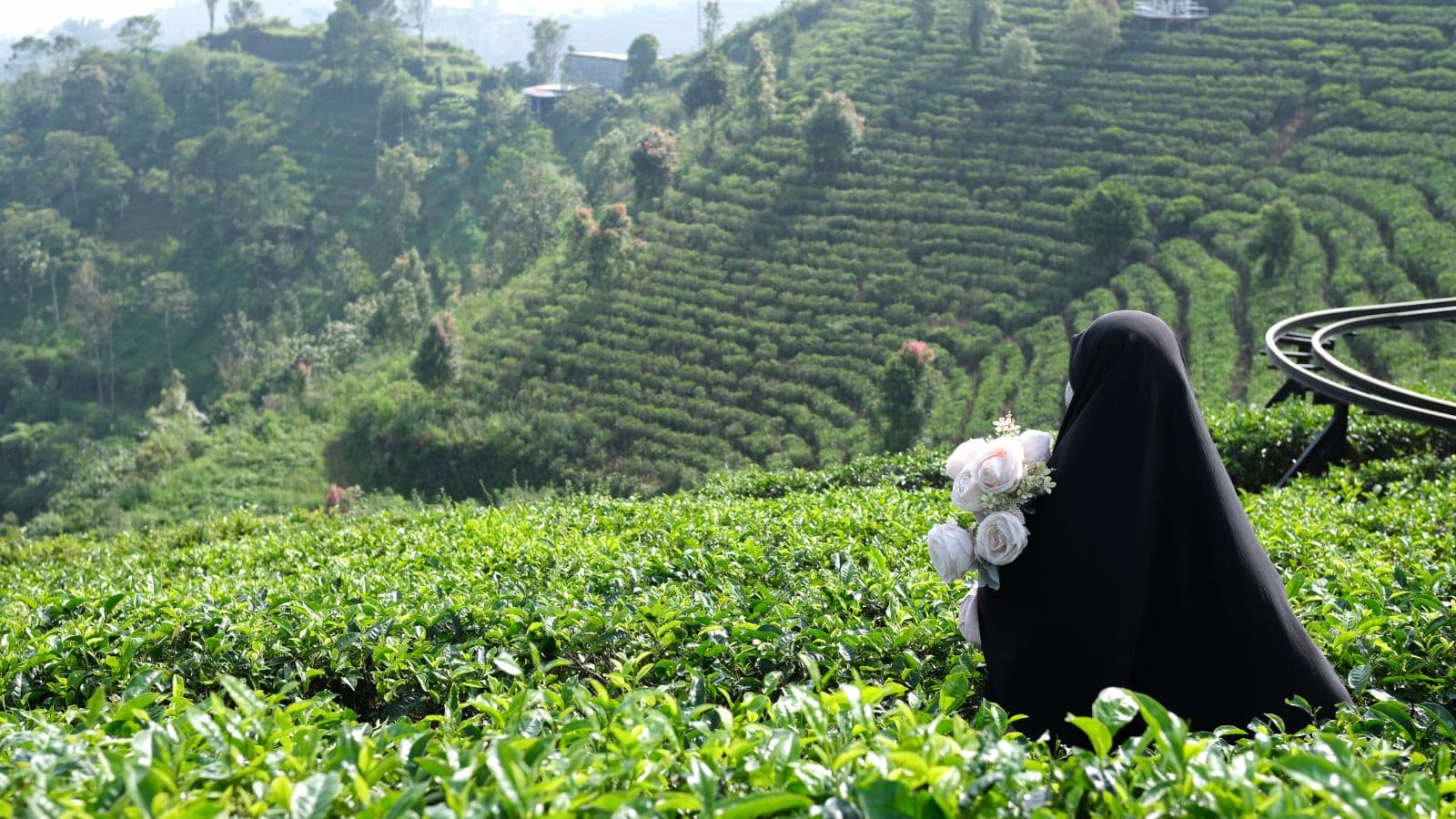 Femme voilée vue de dos assise devant un paysage verdoyant