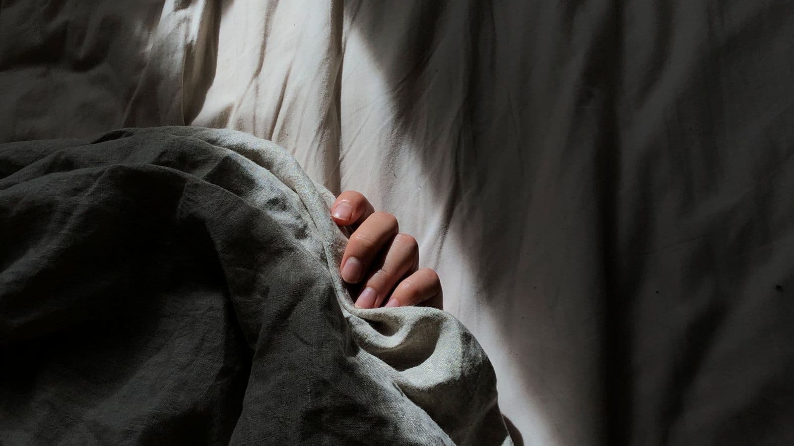 Main reposant sous une couverture dans un lit