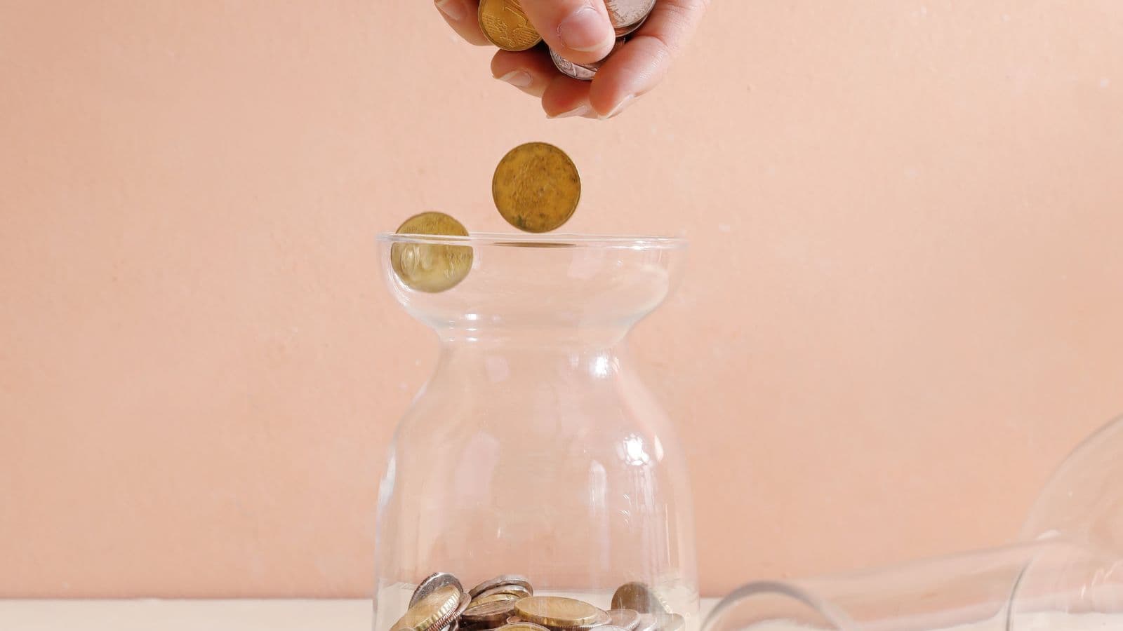Main déposant des pièces dans un bocal transparent