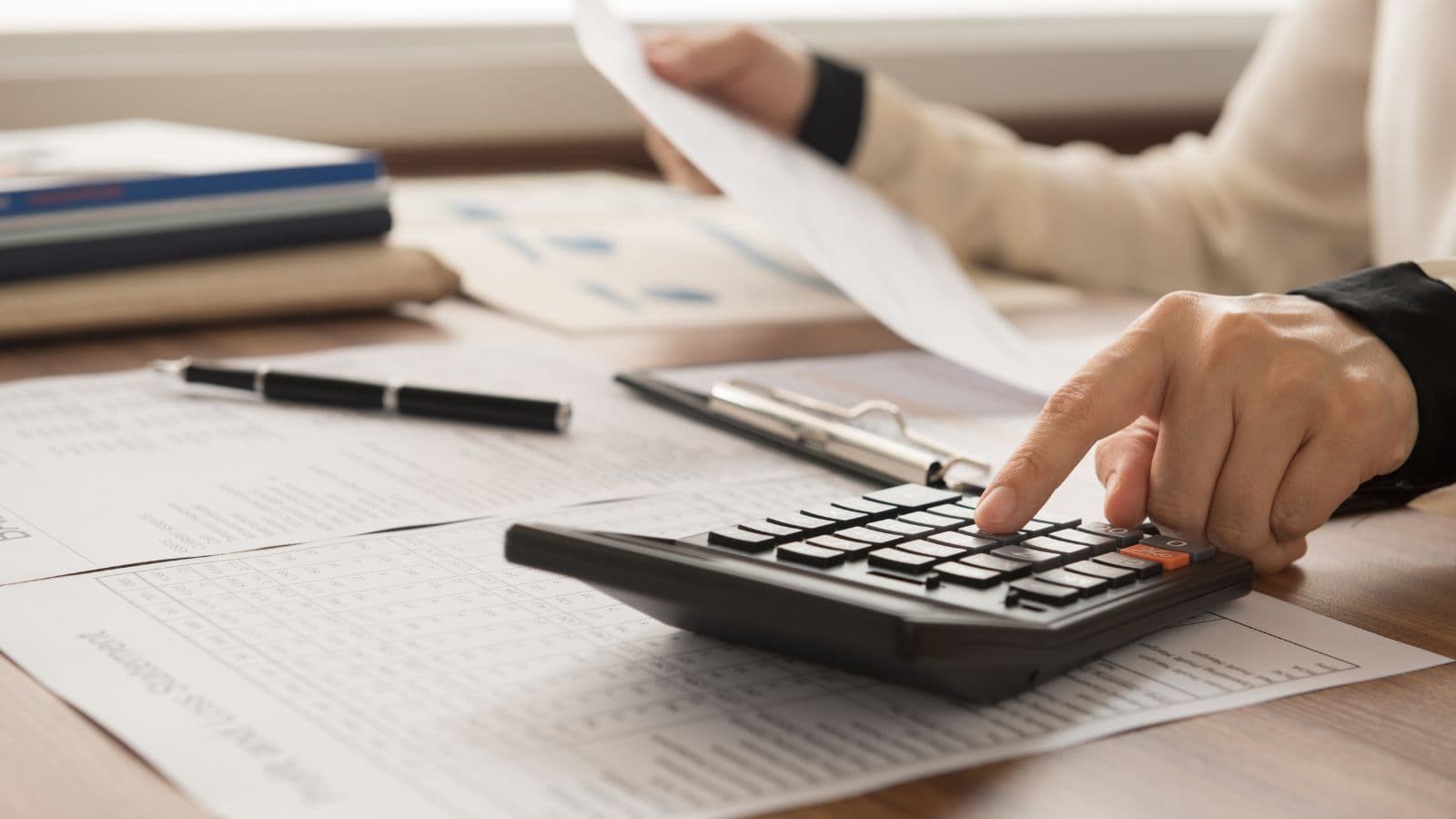 Main utilisant une calculatrice au-dessus de documents comptables