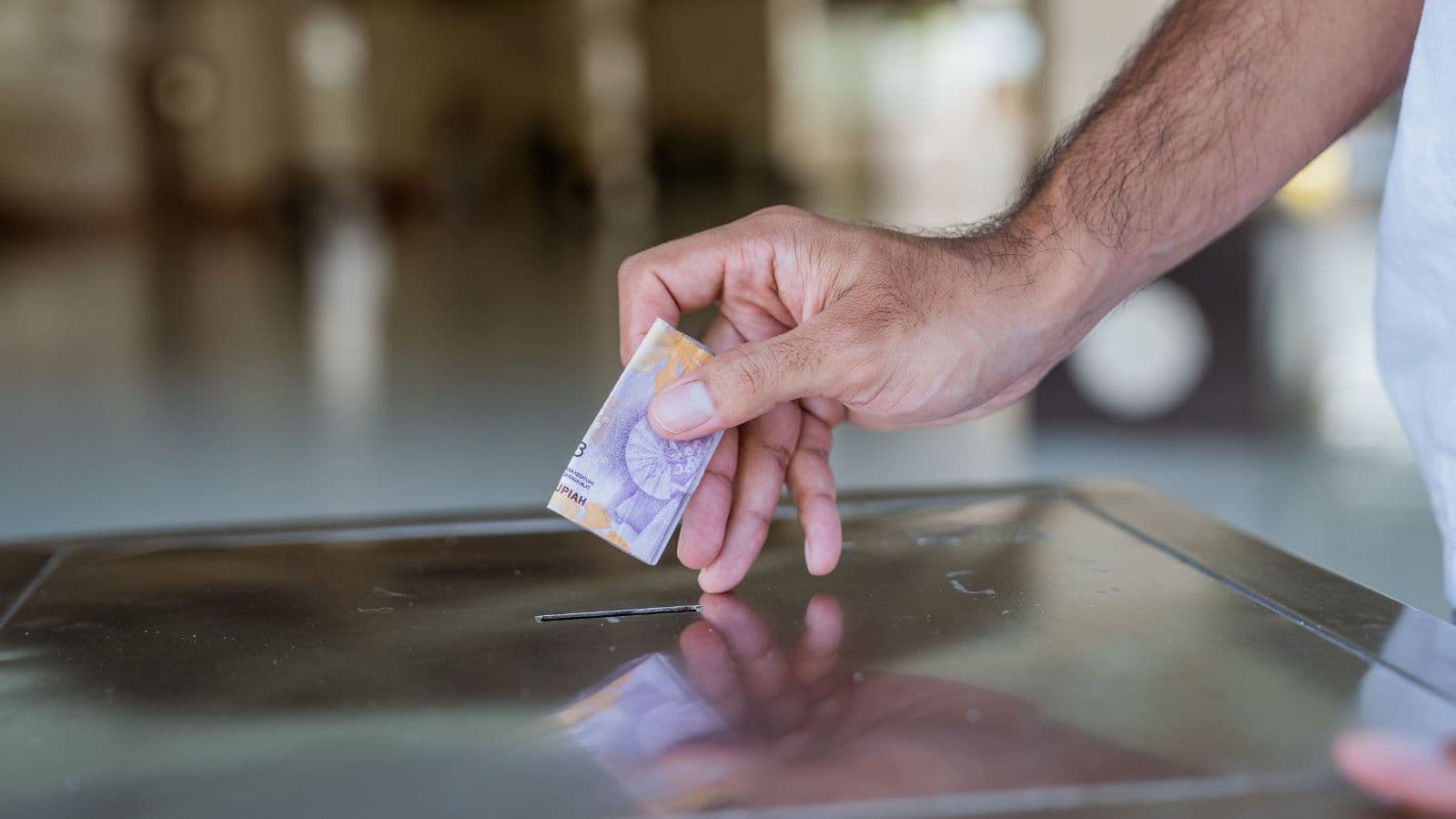 Main déposant un billet dans une boîte de dons