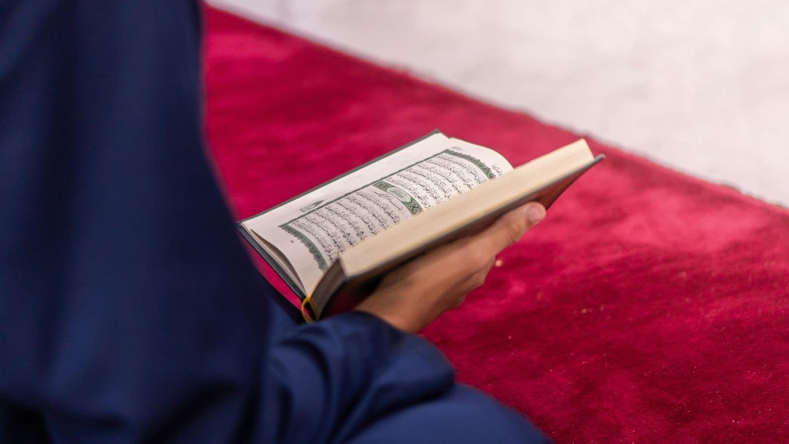 Personne assise lisant un Coran sur un tapis rouge