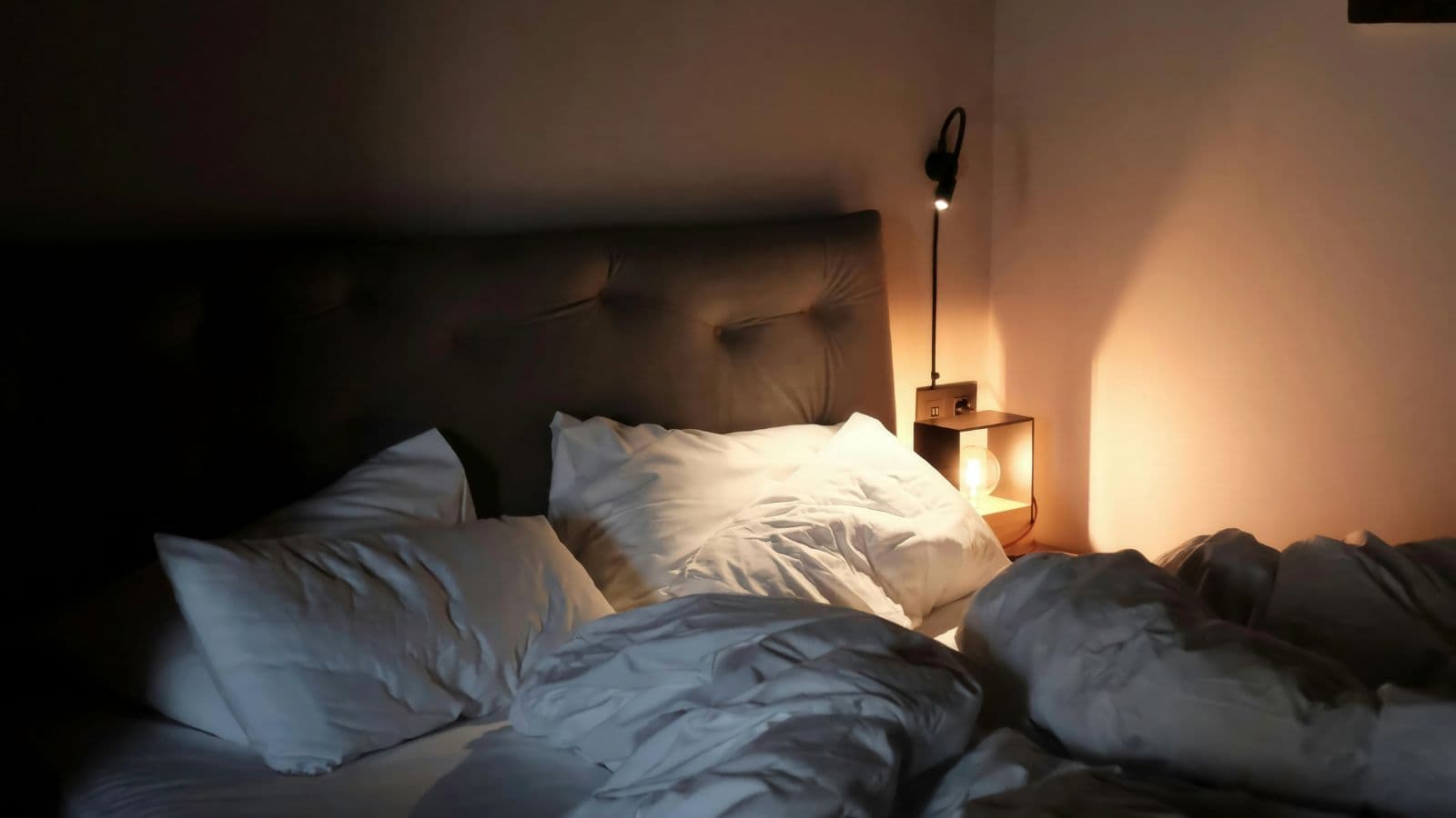 Lit défait dans une chambre éclairée par une lampe